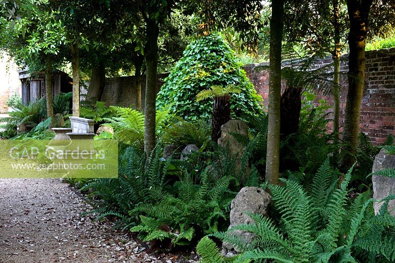 Jardin à feuillage vert avec un siège en pierre devant une pyramide couverte de lierre tous sous des arbres à baldaquin surélevé - Seend, Wiltshire