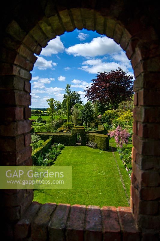 Vue sur jardin et haie par fenêtre en arc de brique, Stone House Cottage Garden and Nusery, nr Kidderminster, Worcestershire.