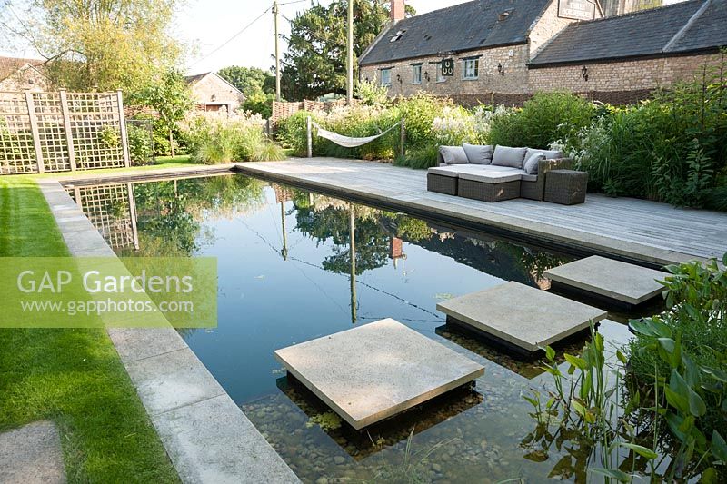 Jardin de la piscine avec étang de baignade, terrasse en bois, hamacs et sièges entourés de plantations naturalistes. Ancien presbytère, Batcombe, Somerset, UK