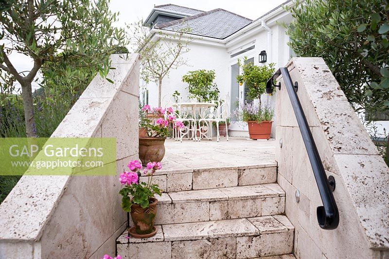 Les marches et la terrasse sont en travertin blanc, avec des pots de pélargoniums roses et d'agrumes ajoutant une touche méditerranéenne. Parc-Lamp, Ruan Lanihorne, Truro, Cornwall, UK