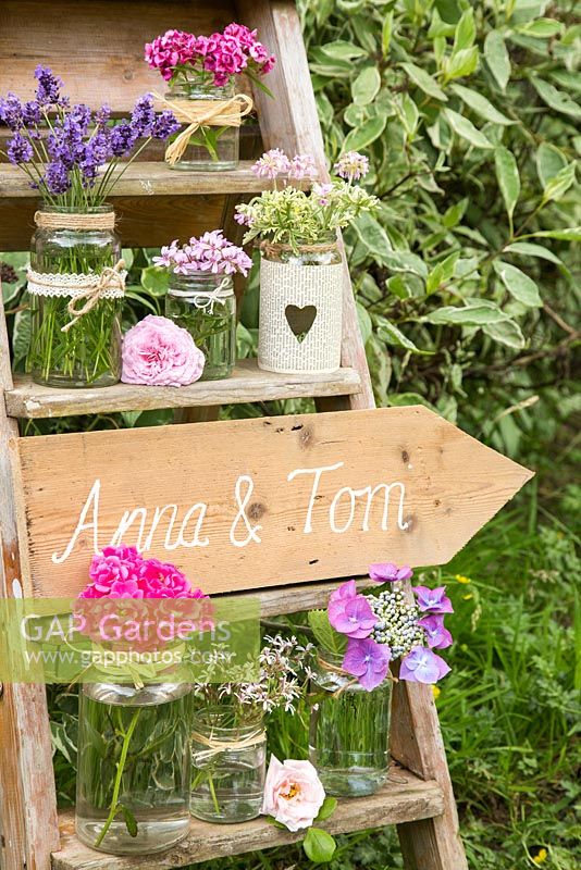 Signe de mariage sur une échelle accompagnée de fleurs d'hortensia, Lavandula, Pelargoniums parfumés, Rosa et Dianthus barbatus.