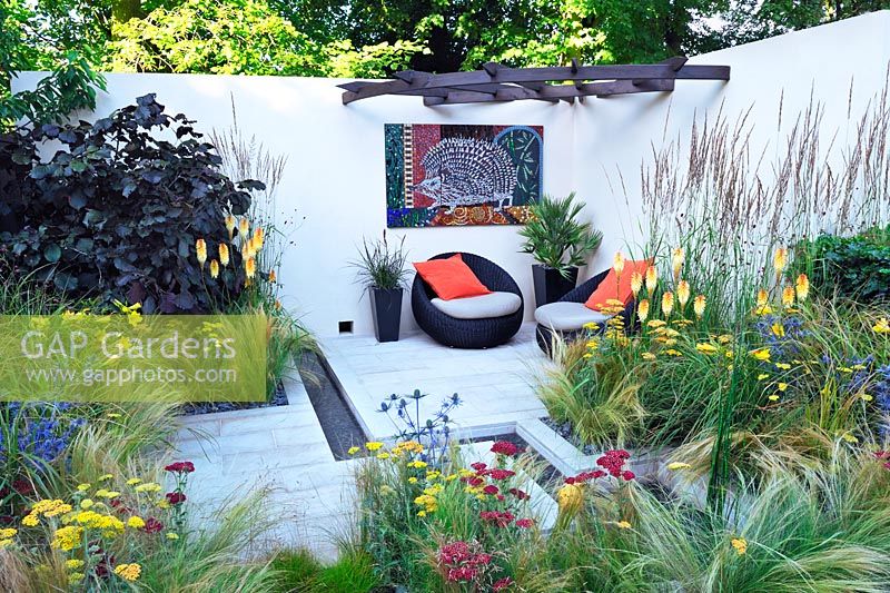 Hedgehog Street. Jardin de la cour, chaises contemporaines avec coussins. Kniphofia, stipa, calamagrostis, achillea