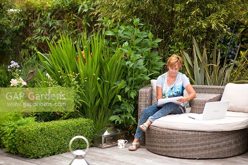 La jardinière Angie Barker dessine dans son jardin des plantations de Phormiums, Crocosmia 'Lucifer' et Lilies retenues par une haie basse de Buxus sempervirens