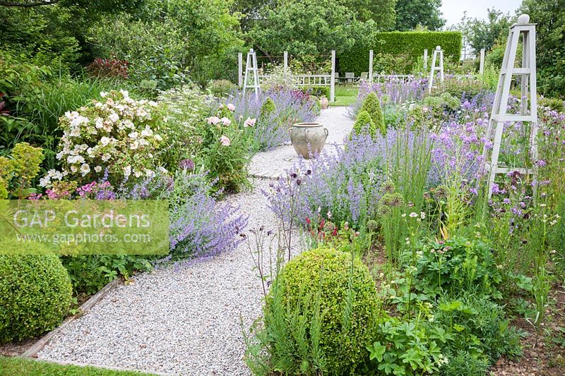 Un jardin fleuri planté de vivaces herbacées et d'obélisques en bois blanc pour une structure toute l'année.