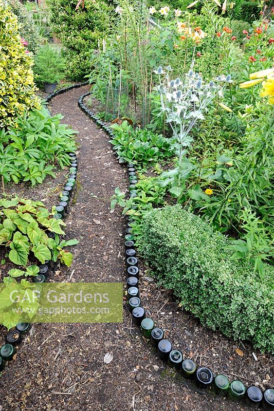 Chemin de jardin bordé de bouteilles menant à travers un parterre d'arbustes et de fleurs, Norfolk, Angleterre, juillet