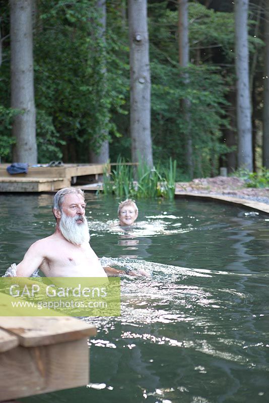 Couple nageant dans leur étang de baignade naturel et la forêt au-delà