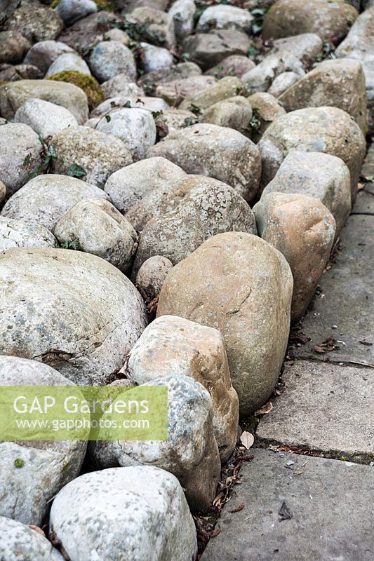 De gros cailloux, serrés les uns contre les autres, utilisés comme paillis dans un jardin à la française.