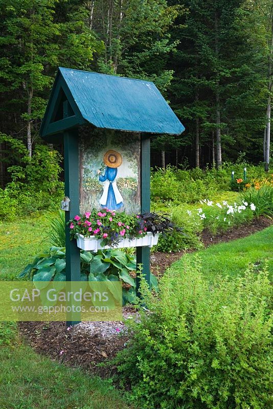 Spiraea x bumalda 'Goldmound' - Arbuste à Spirée, Hosta - 'Blue Blazes' à la base d'une tonnelle en bois ornée d'une peinture acrylique d'une jeune jardinière et d'une boîte d'Impatiens roses plantés dans un jardin de campagne en été, Jardin des Mesanges jardin, Québec, Canada