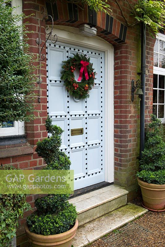 Belle vieille porte d'entrée décorée d'une couronne de Noël traditionnelle et durable faite d'épicéa, avec des cynorrhodons rouges, des citrouilles séchées et du ruban.