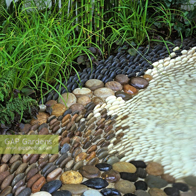 Une petite piscine claire est bordée de galets de couleur claire et foncée incrustés dans du béton et a continué à monter jusqu'à ce qu'elle soit ramollie par une plantation marginale.