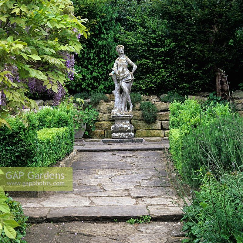 La statue en pierre italienne d'un jeune noble crée un point focal sur les parterres de fleurs à l'if du jardin formel de Casita.