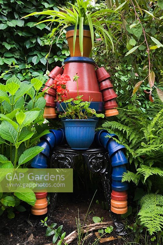Sculpture de forme humaine faite de pots de fleurs bleu, rouge et terre cuite dans un jardin urbain en été, Québec, Canada