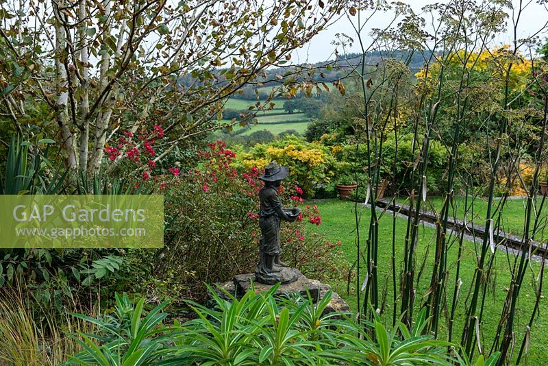 Une vue d'une statue entourée d'Euphorbia mellifera, fenouil et Rosa Hertfordshire. Au-delà, un ruisseau mène l'œil à la vue de la vallée de l'Axe.