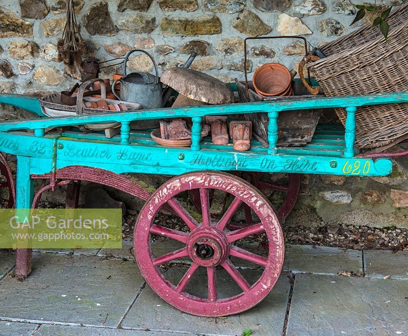 Un chariot à main peint coloré rempli d'accessoires de jardinage.