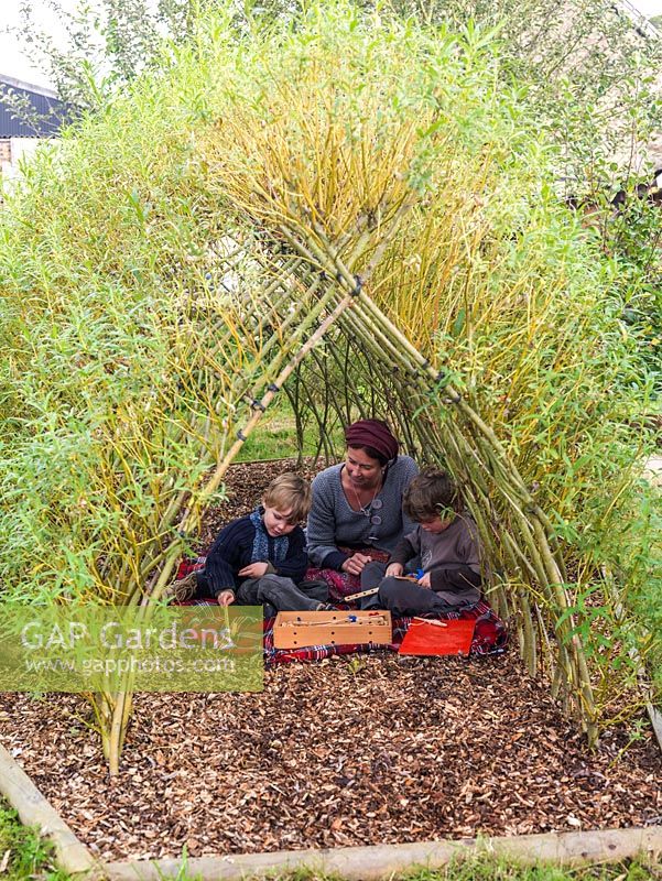 Les frères Jacob et Loui avec leur mère, Ali Rose, jouent sur le sol à l'ombre d'un tunnel tressé de Salix viminalis - saule vivant.