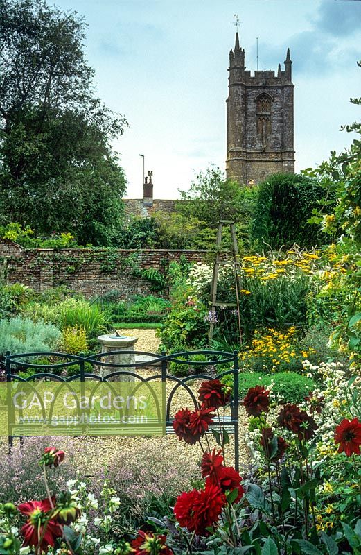 Vue sur jardin formel avec banc en fer forgé peint en bleu, vieux cadran solaire, chemins de gravier, roses, vivaces herbacées - Cerne Abbas, Dorset