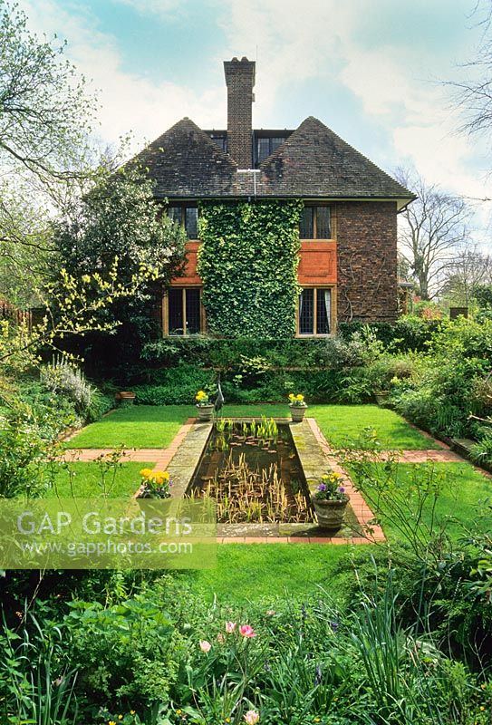 Jardin en contrebas formel avec étang rectangulaire situé dans la pelouse. Détails en pierre et brique. Panneau de lierre soigneusement coupé sur le mur de la maison.