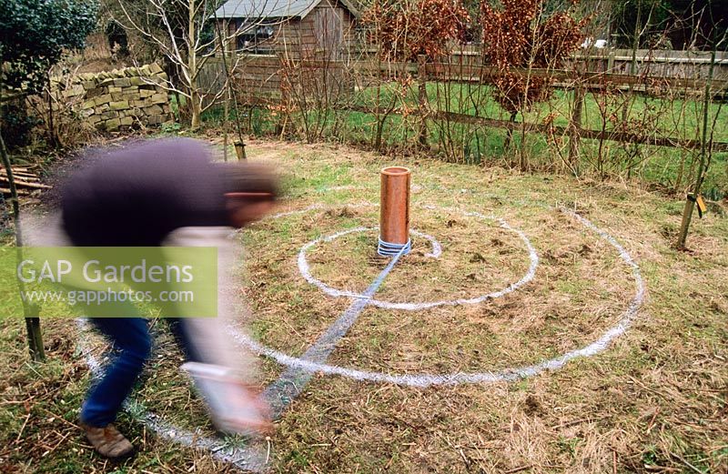 Homme traçant une spirale sur l'herbe rugueuse en automne avec un pot de peinture marqueur afin de planter une caractéristique de spirale de crocus pour le printemps