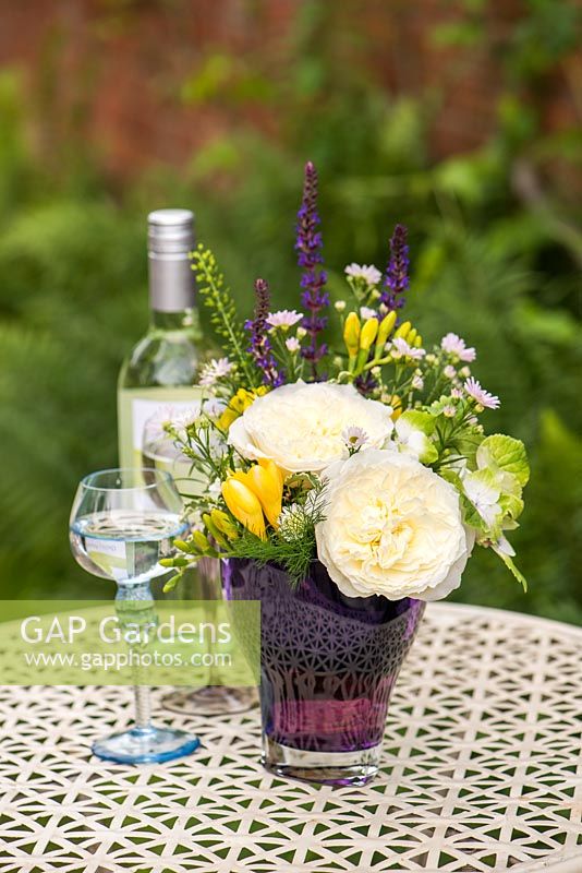 Un arrangement de fleurs coupées sur une table de jardin dont Rosa 'Patience'