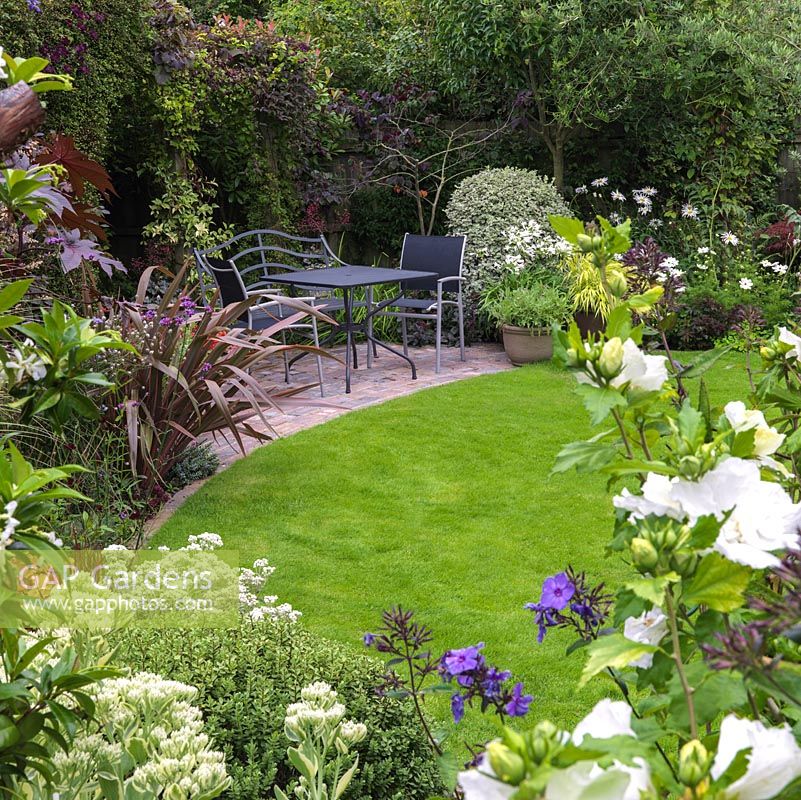 Petit jardin à l'arrière avec pelouse centrale, coin salon pavé et parterres de fleurs mixtes