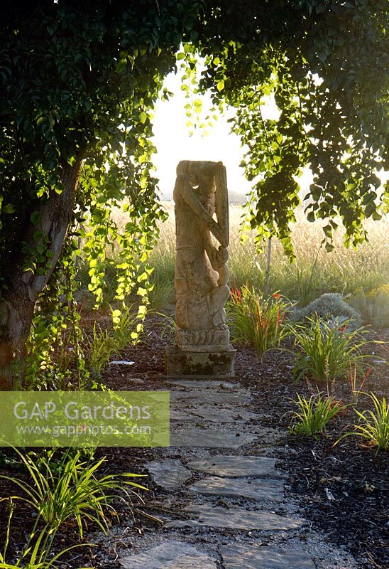 Une sculpture en pierre située au bout d'un long chemin de pierre. Parmi un parterre de graminées mixtes nouvellement plantées. Domaine de Cambou, Verfeil, Haute-Garonne, Midi Pyrénées, France.