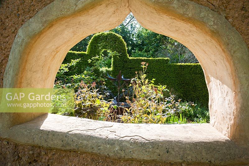 Pièce d'eau en métal conçue et réalisée par Michael Chaikin vue à travers une fenêtre dans le mur en torchis. Jardin planté de rodgersias, d'hamamélis, de roses et d'amsonia. Ferme Caervallack, St Martin, Helston, Cornwall, UK