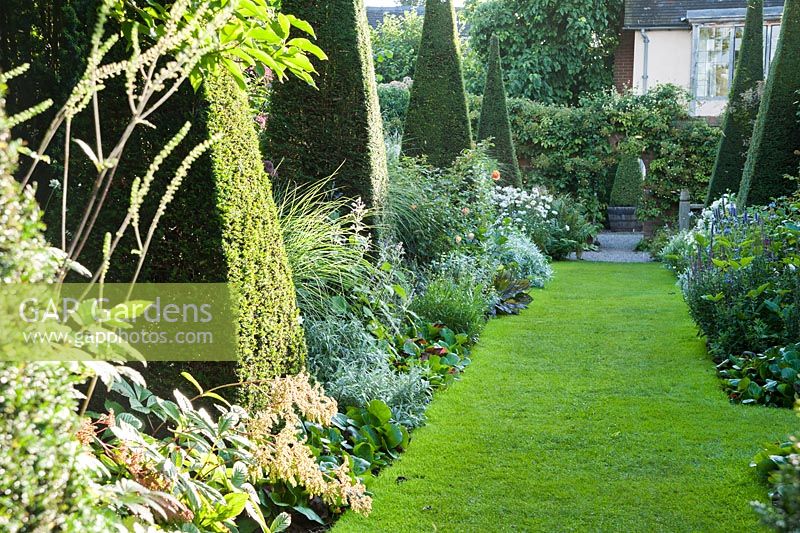 Le Yew Walk dominé par dix hautes flèches d'ifs entrecoupées de plantations en bleu, argent et blanc avec des éclairs d'abricot. Wollerton Old Hall, nr Market Drayton, Shropshire, Royaume-Uni