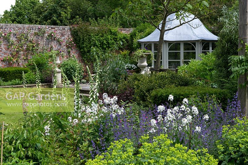 Un jardin clos avec une maison d'été en forme de dôme et un parterre de fleurs mélangé planté de digitale, de roquette, de menthe et d'alchémille.