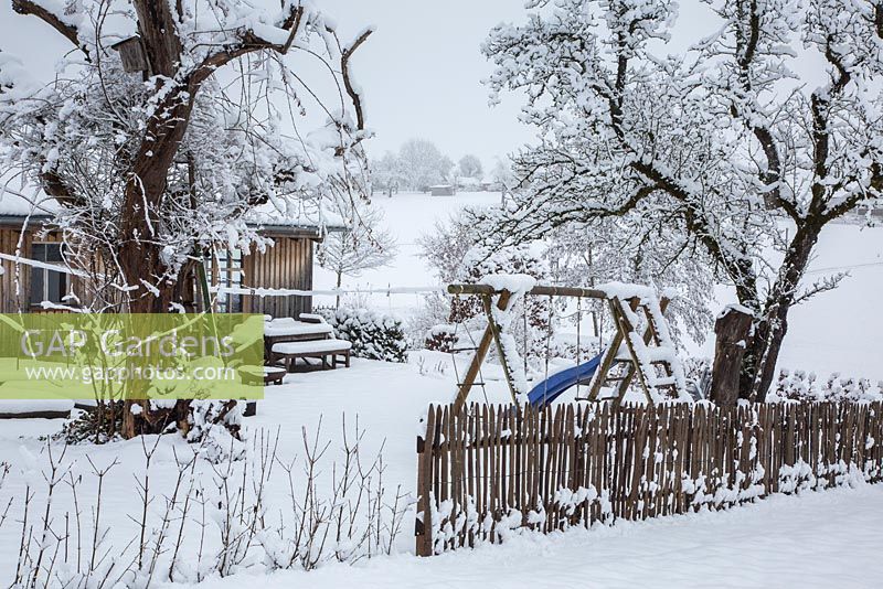Scène d'hiver avec piquet de grève en bois, équipement de jeu pour enfants, arbres et cabanon