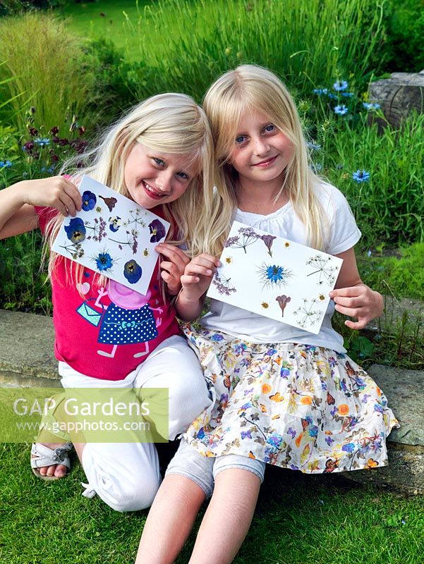 Les petites filles brandissant des cartes créées à partir de fleurs pressées qu'elles ont cueillies et se sont pressées pour en faire une carte de fête des mères.