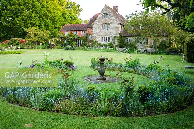 Jardin à la française en face d'un manoir jacobin de grade II, avec des parterres de fleurs circulaires plantés de verbascum, d'iris et de myosotis. King John's Nursery, Etchingham, East Sussex, Royaume-Uni