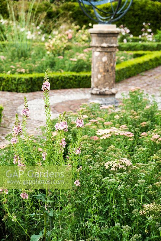 Les plates-bandes bordées de fleurs dans le jardin clos contiennent un mélange d'achillea, verbascum et Stipa gigantea, avec cadran solaire au centre. Beaminster Manor, Beaminster, Dorset, Royaume-Uni