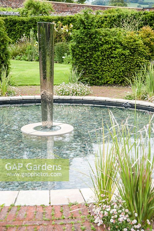 Piscine circulaire avec élément d'eau dans le jardin clos conçu par Lesley Cooper, avec Erigeron karvinskianus et dierama autour du bord. Beaminster Manor, Beaminster, Dorset, Royaume-Uni
