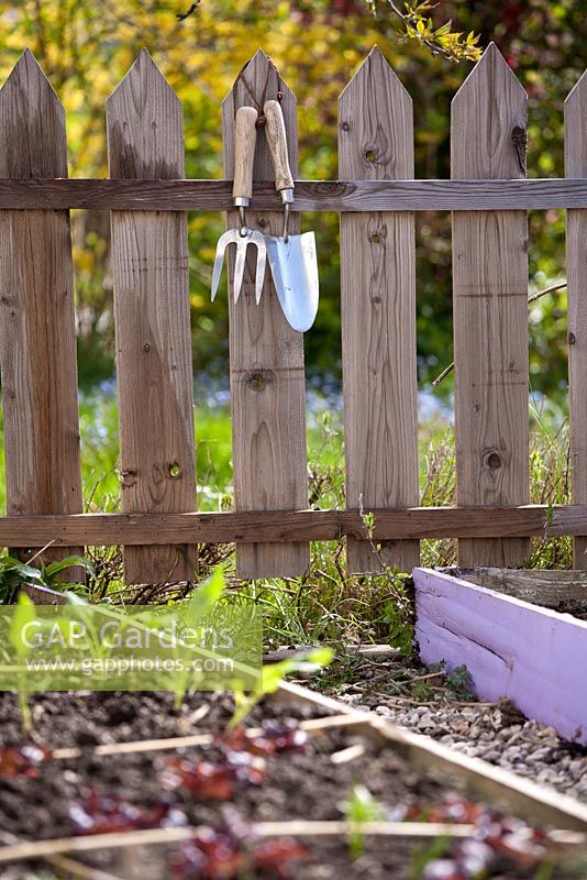 Fourchette à main et truelle accrochée à une clôture à côté des parterres de légumes.