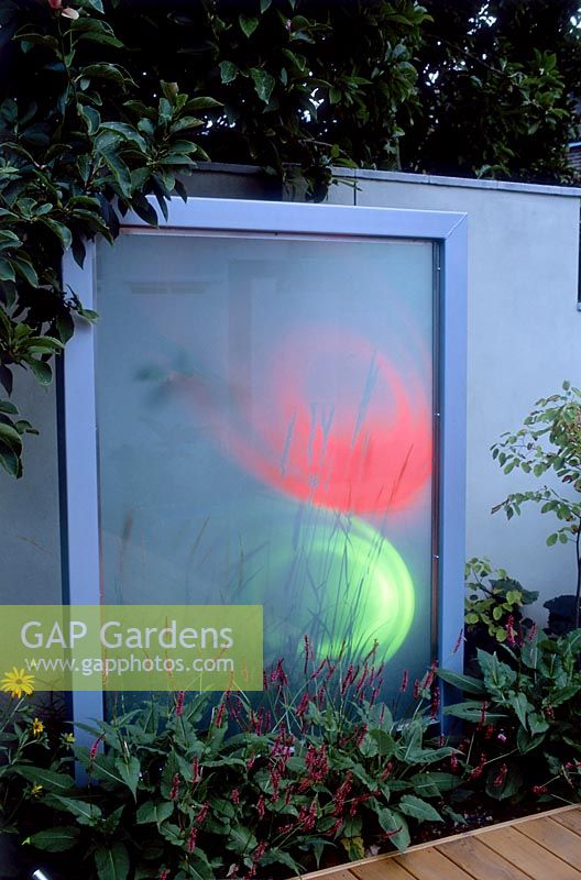 Un écran en verre dépoli avec un éclairage coloré dans un jardin de ville moderne conçu par Paul Dracott, Londres.