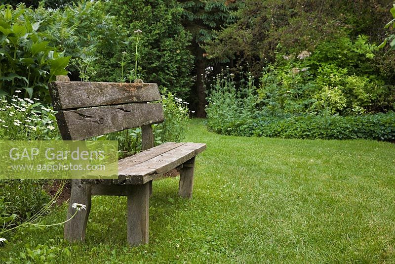 Ancien banc en bois sur pelouse verte dans un jardin privé en été