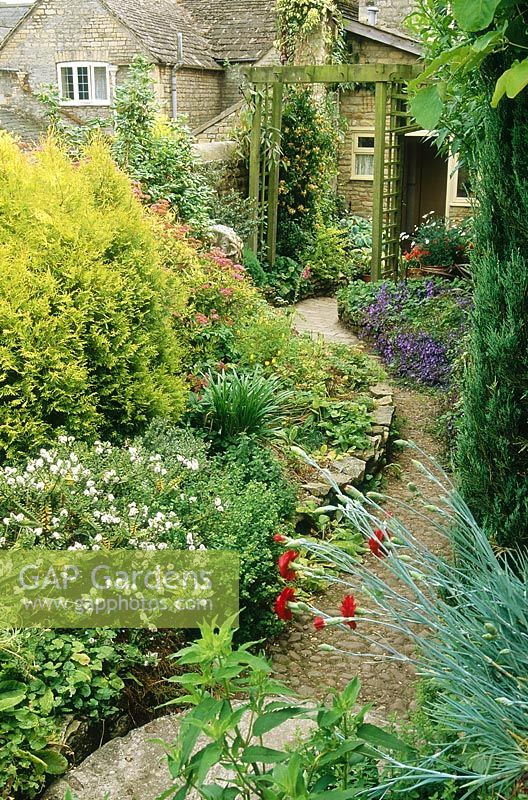 Jardin de ville étroit avec parterre de fleurs, arche en bois et mur en pierre. Les plantes comprennent l'hébé, le conifère et le dianthus, King's Cliffe, Northamptonshire