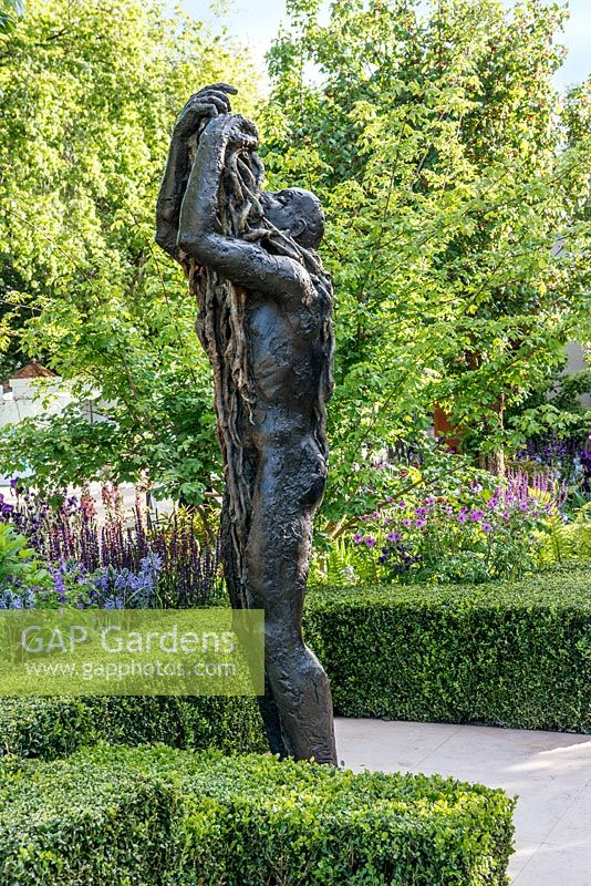 Le jardin Morgan Stanley Healthy Cities. Sculpture en bronze d'une figure avec boîte de couverture et parterres de fleurs herbacées en arrière-plan
