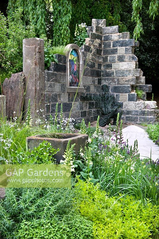 Ruine d'église aux murs de pierre, chemin, auge et plantes de jardin, y compris Digitalis purpurea - digitale et herbes. The Evaders Garden par Chorley Council. RHS Chelsea Flower Show, 2015.
