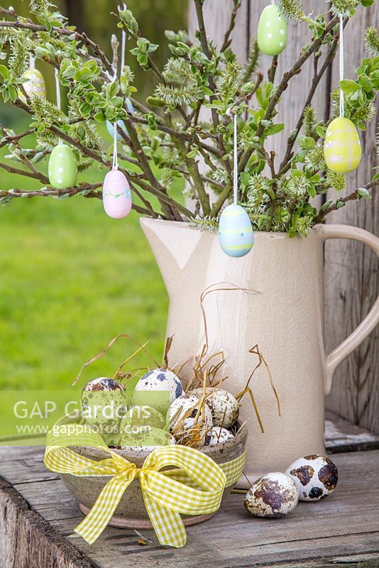 Oeufs décoratifs suspendus au feuillage frais du printemps, accompagnés d'un bol d'oeufs de caille et vue sur le jardin