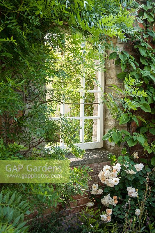 Fenêtre décorative dans un mur de jardin encadré de Xanthocerus sorbifolium