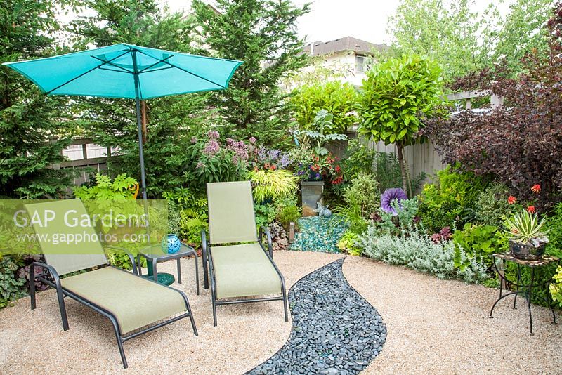 Fauteuils inclinables et parasol dans le jardin de la cour. Parterres de fleurs et pots mixtes. Agave schidigera 'Shiro Ito No Ohi', Epilobium, Parahebe, Hakonechloa, Ipomoea