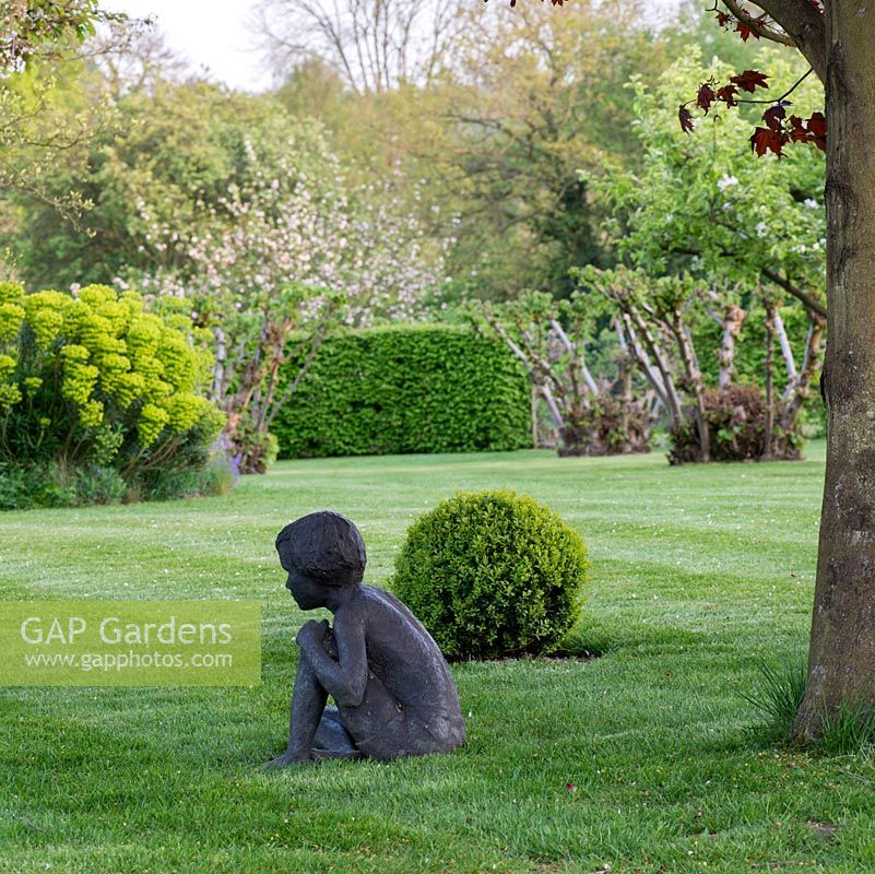 Figurine d'enfant, sculptée par Jenny Wynn Jones, dans le jardin du printemps, reposant sur la pelouse par une bille.