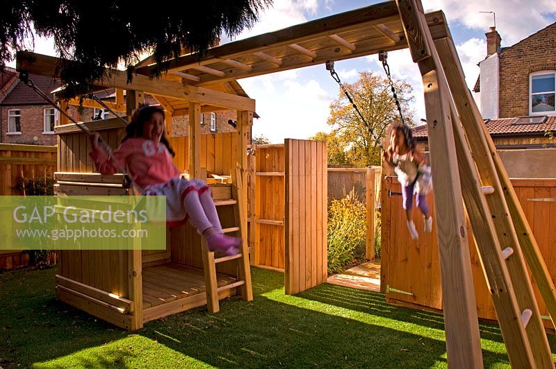 Fille sur balançoire. Aire de jeux pour enfants avec cadre d'escalade en bois. Petit jardin urbain contemporain urbain. Jardin Ansari, Harrow
