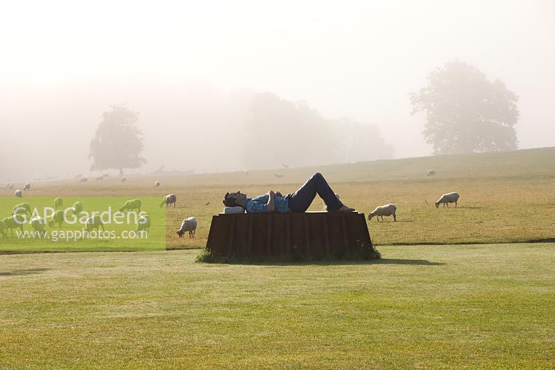 La pelouse principale en brume avec sculpture en bronze et acier corten par Sean Henry. Moutons paissant dans le champ au-delà.