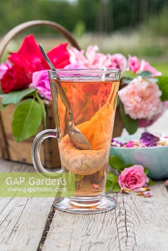 Un verre de thé rose avec un trug de roses coupées et de pétales