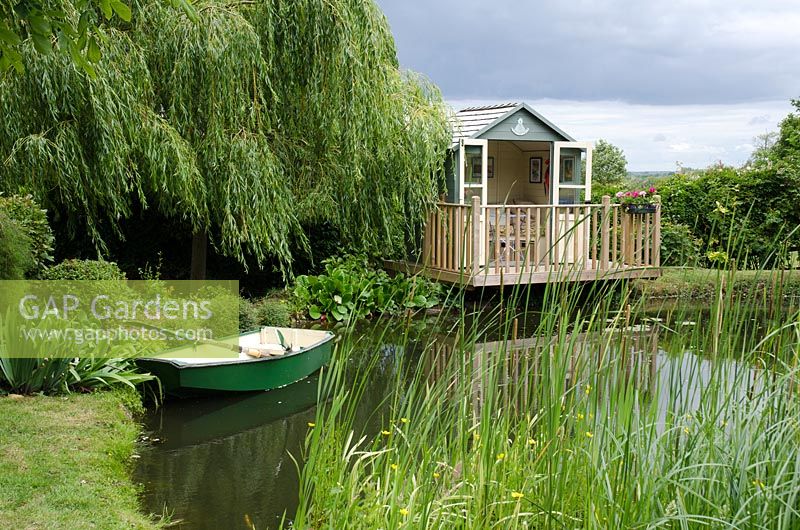 Pavillon à côté de Salix babylonica 'Pendula' donnant sur un étang avec un bateau