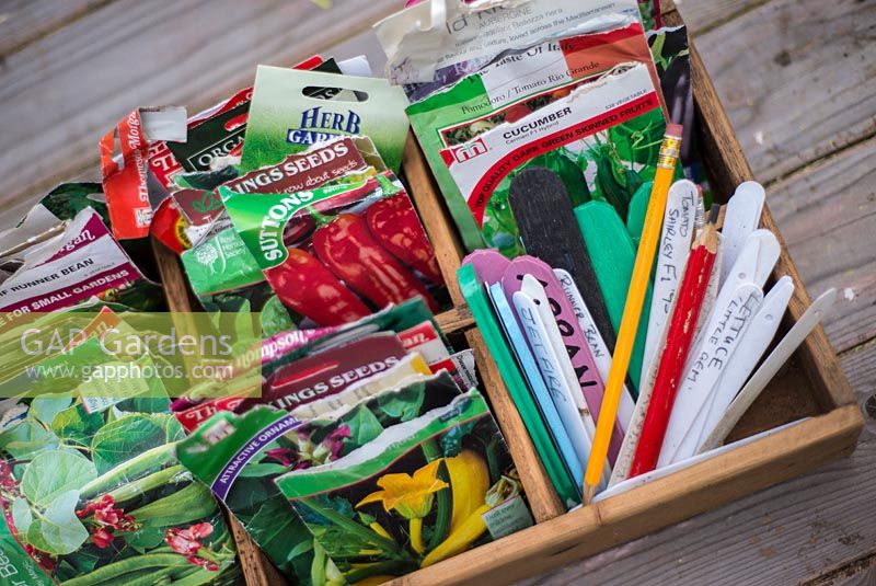 Boîte en bois partitionnée avec des sachets de graines, diverses étiquettes et crayons.