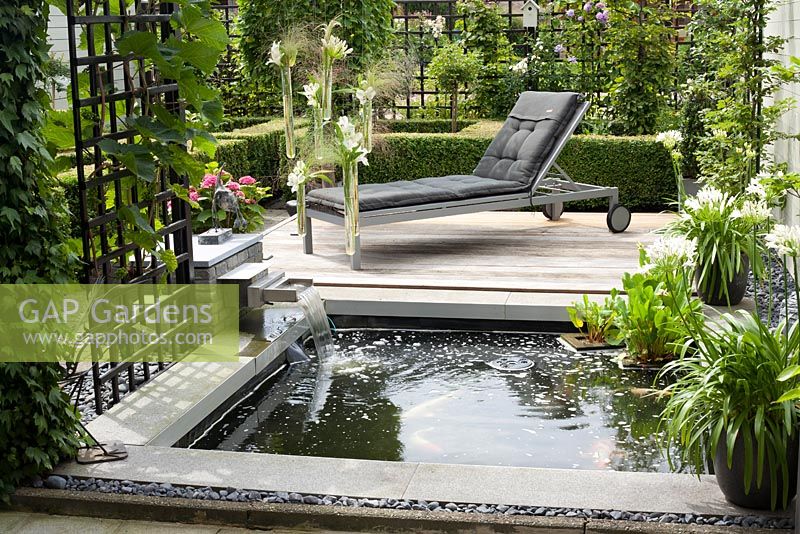 Petit étang rectangulaire avec cascade et terrasse en bois. Agapanthus orientalis Blanc en pot. Famille Fabry - Mathijs. Belgique
