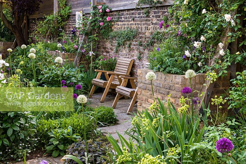 En lit central ensoleillé: alliums violets et blancs, Mathiasella burpleuroides 'Green Dream', sedum, scabious, pivoines et iris. De plus en plus dans des parterres surélevés sur le mur droit, géranium Rozanne, lavande et roses.